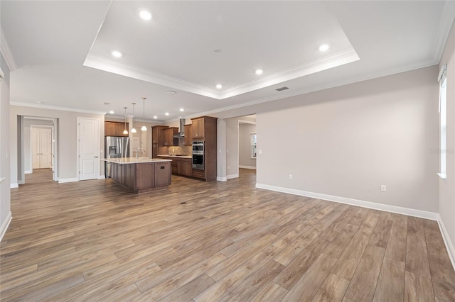 unfurnished living room with a tray ceiling, baseboards, light wood finished floors, and recessed lighting