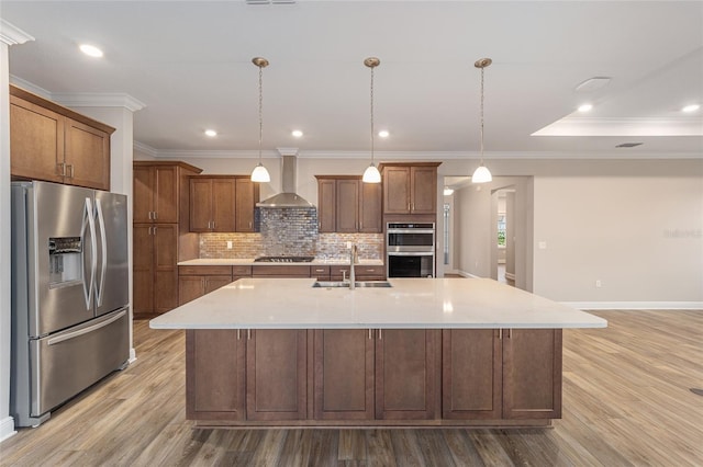 kitchen featuring stainless steel appliances, tasteful backsplash, light wood-style flooring, a sink, and wall chimney range hood