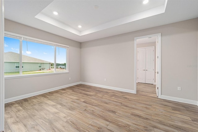 empty room featuring light wood-type flooring, a tray ceiling, baseboards, and recessed lighting