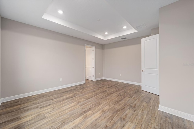 unfurnished room with baseboards, light wood-type flooring, a raised ceiling, and recessed lighting