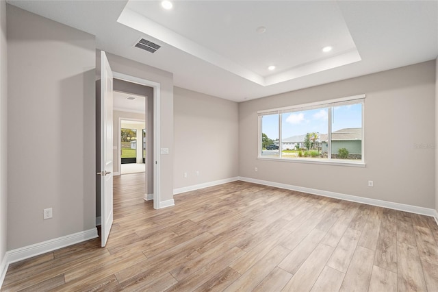 empty room featuring a tray ceiling, light wood finished floors, recessed lighting, visible vents, and baseboards