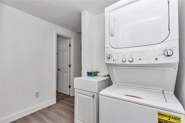 laundry room with stacked washing maching and dryer, cabinet space, baseboards, and light wood-style floors