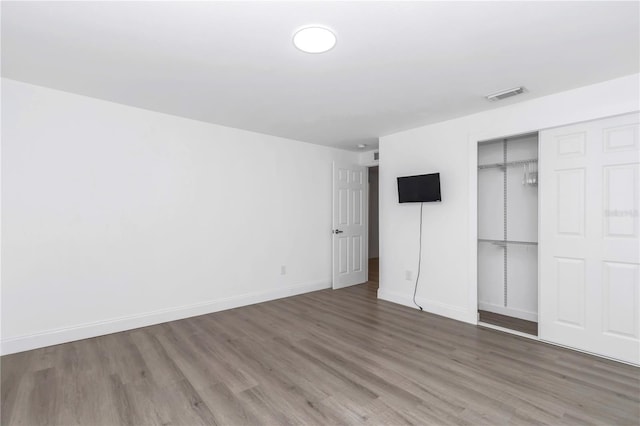 unfurnished bedroom featuring a closet, visible vents, baseboards, and wood finished floors