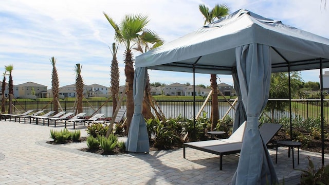 view of patio / terrace featuring a gazebo, a water view, fence, and a residential view