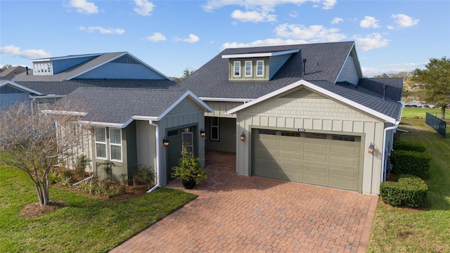 view of front facade with a garage, roof with shingles, decorative driveway, board and batten siding, and a front yard