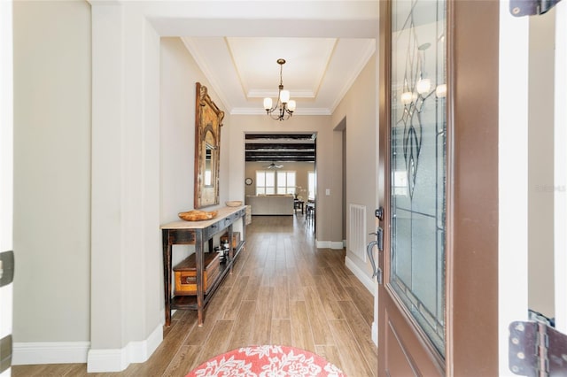 foyer featuring baseboards, light wood-type flooring, a tray ceiling, an inviting chandelier, and crown molding