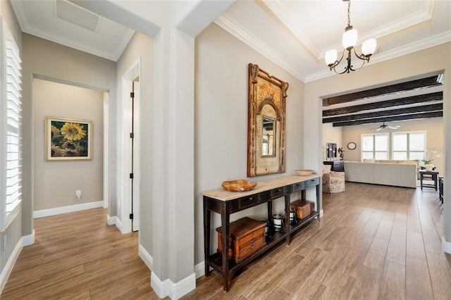 hallway with light wood-style flooring, beam ceiling, ornamental molding, and baseboards