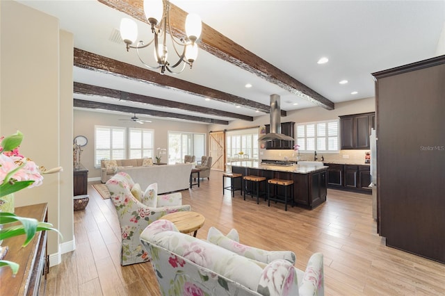 living area with light wood-style floors, ceiling fan with notable chandelier, beamed ceiling, and a barn door