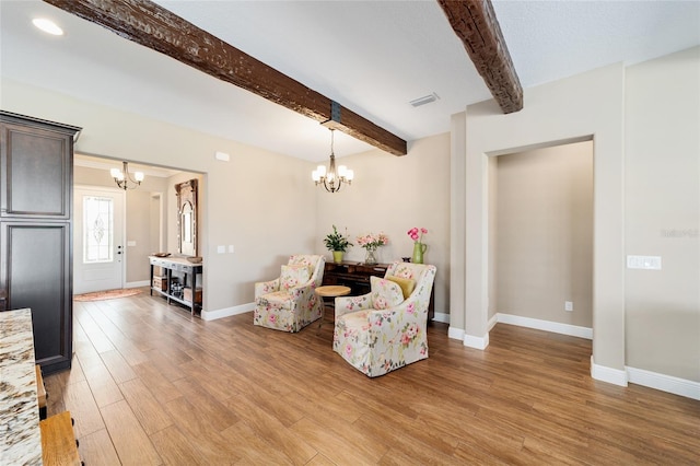 sitting room featuring a notable chandelier, light wood finished floors, visible vents, beamed ceiling, and baseboards