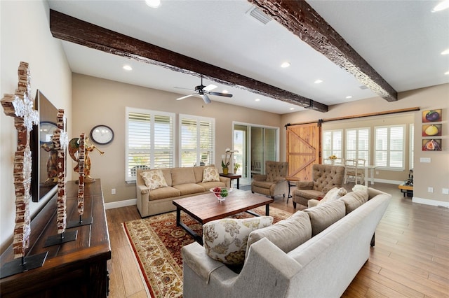 living area featuring beam ceiling, light wood-style flooring, baseboards, and a barn door