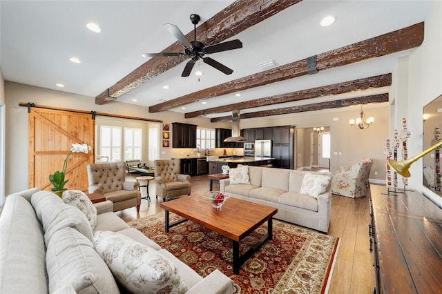 living area featuring a barn door, recessed lighting, ceiling fan with notable chandelier, beam ceiling, and light wood finished floors