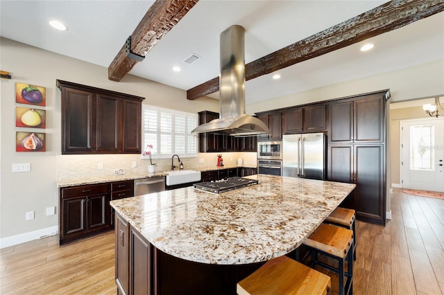 kitchen with island exhaust hood, visible vents, appliances with stainless steel finishes, a sink, and beamed ceiling