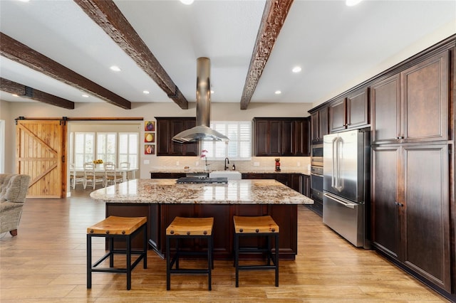 kitchen featuring a barn door, a center island, island exhaust hood, stainless steel appliances, and a kitchen bar