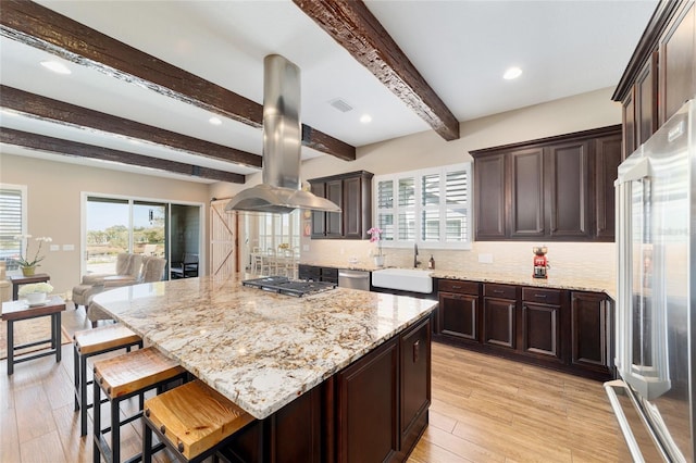 kitchen with light stone counters, stainless steel appliances, a sink, visible vents, and island exhaust hood