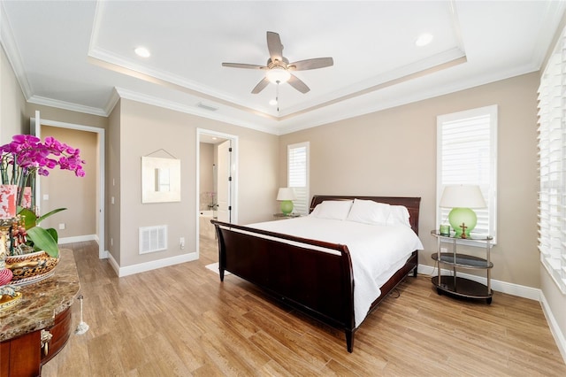 bedroom featuring a tray ceiling, light wood-type flooring, visible vents, and baseboards