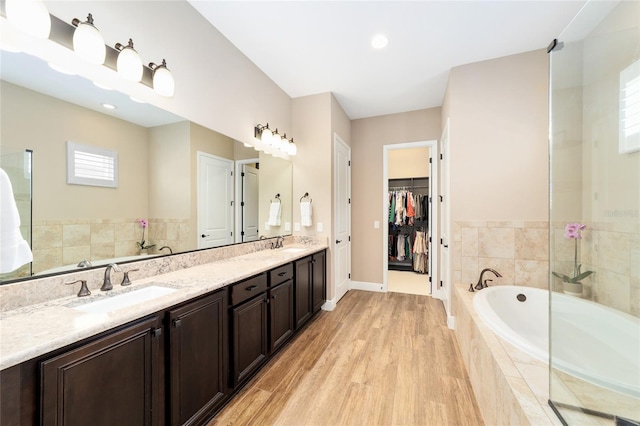 full bath with double vanity, a garden tub, a walk in closet, and a sink