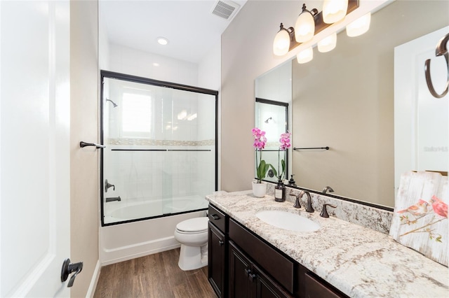 full bathroom with visible vents, toilet, combined bath / shower with glass door, vanity, and wood finished floors