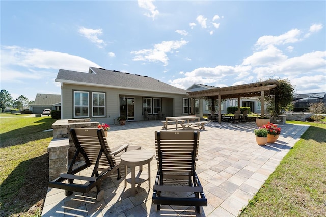 rear view of house with a shingled roof, a pergola, a lawn, and a patio