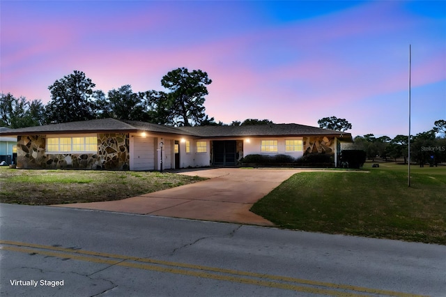 ranch-style house featuring stone siding, concrete driveway, a lawn, and an attached garage