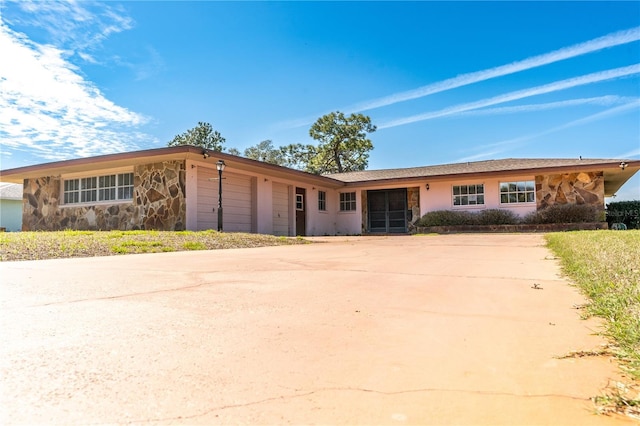 ranch-style home with an attached garage, stone siding, and driveway