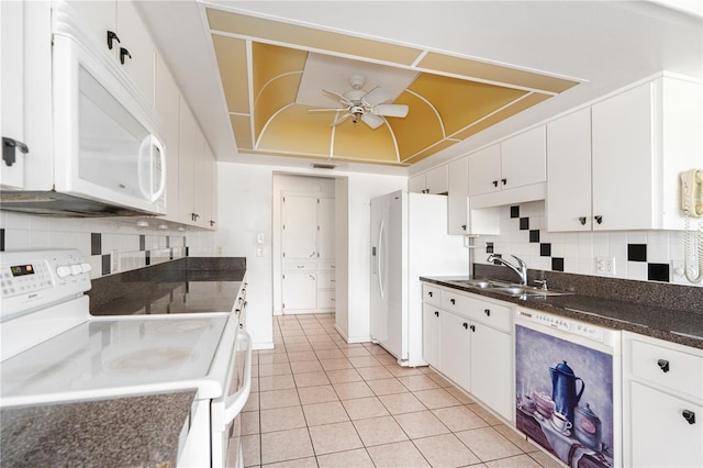 kitchen featuring dark countertops, a raised ceiling, a sink, ceiling fan, and white appliances