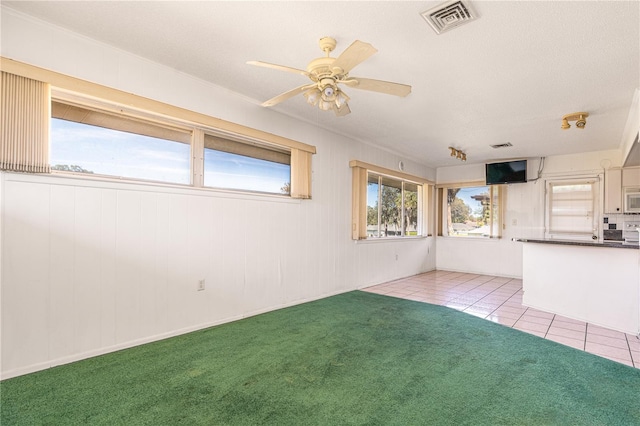 carpeted spare room with visible vents, a ceiling fan, and tile patterned floors