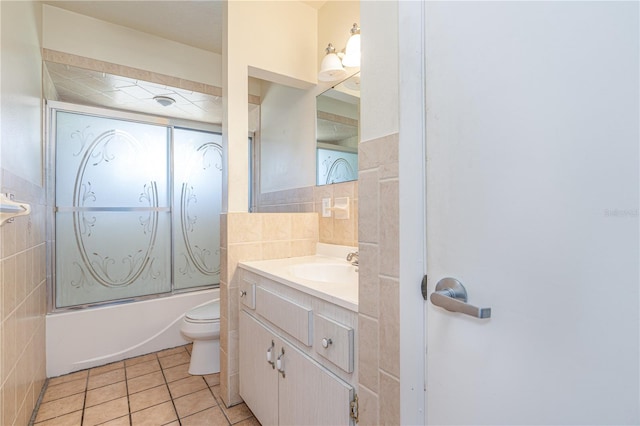 bathroom featuring toilet, vanity, tile walls, combined bath / shower with glass door, and tile patterned floors