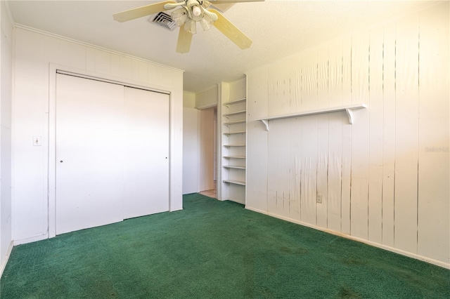 unfurnished bedroom with wooden walls, carpet flooring, ceiling fan, and visible vents