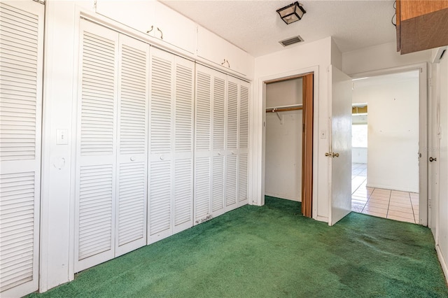 unfurnished bedroom with carpet, visible vents, a textured ceiling, and tile patterned floors