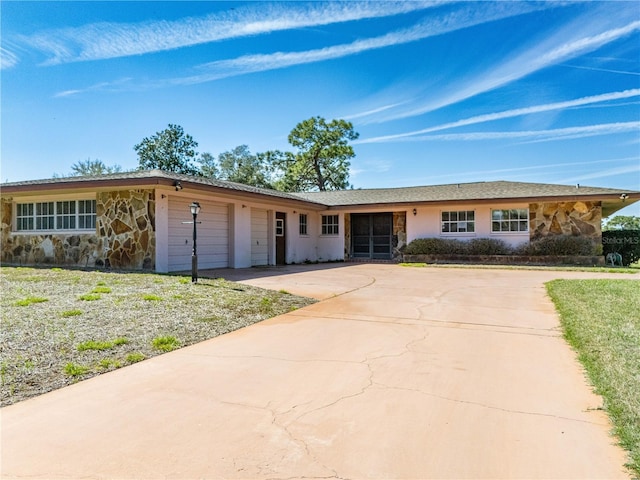 single story home featuring a garage, concrete driveway, and stone siding