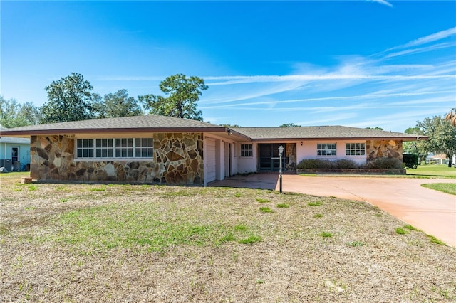 single story home with a front lawn, stone siding, and concrete driveway