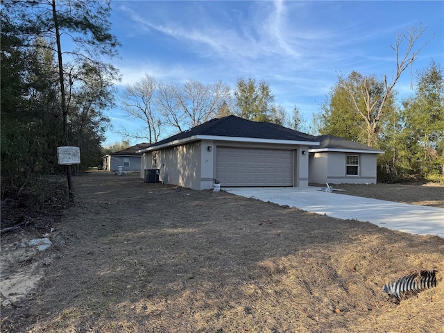 ranch-style house featuring a garage, central AC, concrete driveway, and stucco siding