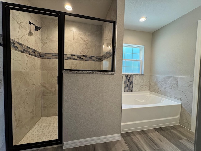 bathroom featuring a textured ceiling, a textured wall, a garden tub, wood finished floors, and a shower stall