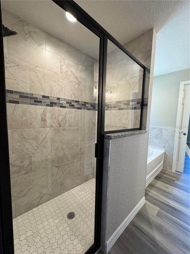 bathroom with a textured ceiling, a textured wall, a garden tub, wood finished floors, and a stall shower