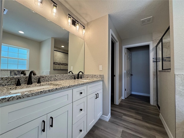 bathroom with wood finished floors, a stall shower, a sink, and visible vents