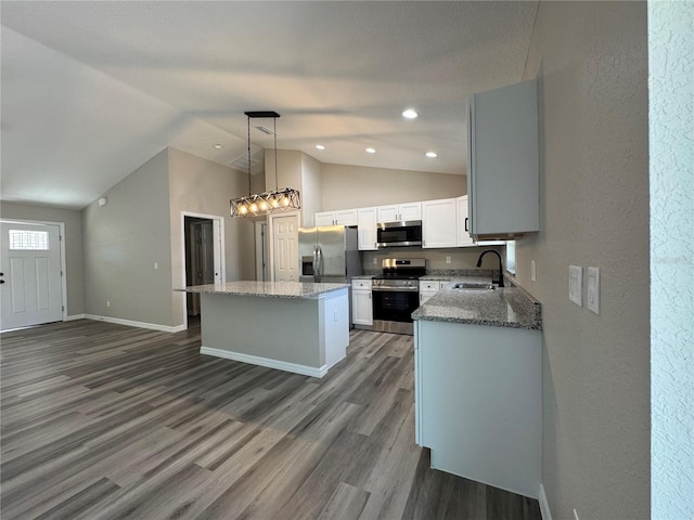 kitchen with a center island, dark wood finished floors, appliances with stainless steel finishes, a sink, and light stone countertops