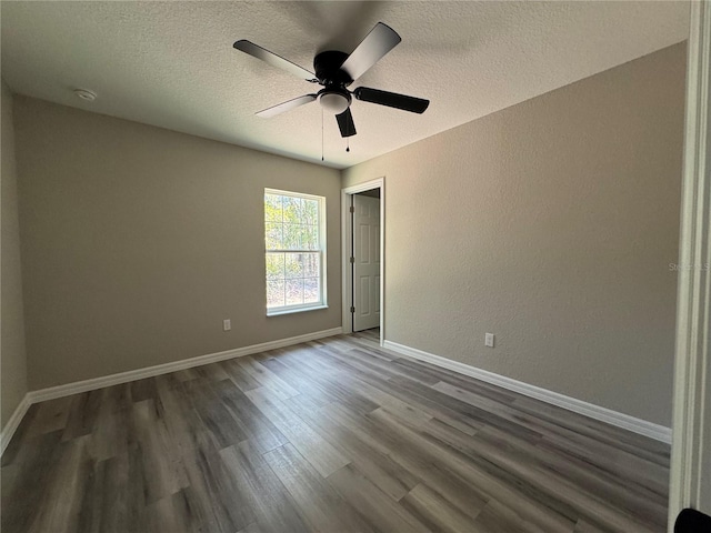 spare room featuring dark wood-style flooring, a textured wall, ceiling fan, a textured ceiling, and baseboards