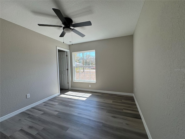 empty room with a textured ceiling, a textured wall, wood finished floors, a ceiling fan, and baseboards