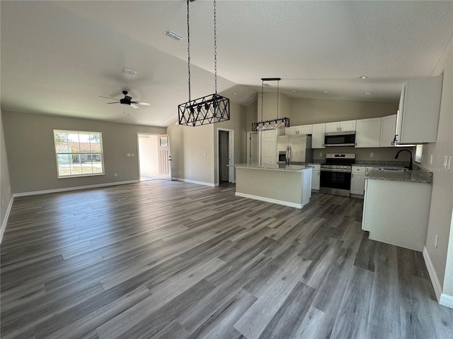 kitchen featuring white cabinets, appliances with stainless steel finishes, open floor plan, hanging light fixtures, and a sink