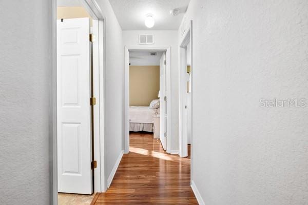 hallway featuring wood finished floors, visible vents, and baseboards