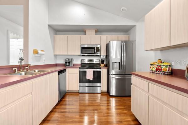 kitchen featuring lofted ceiling, appliances with stainless steel finishes, light brown cabinets, a sink, and wood finished floors