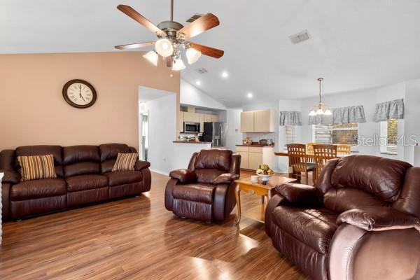 living area with lofted ceiling, recessed lighting, ceiling fan with notable chandelier, visible vents, and light wood finished floors