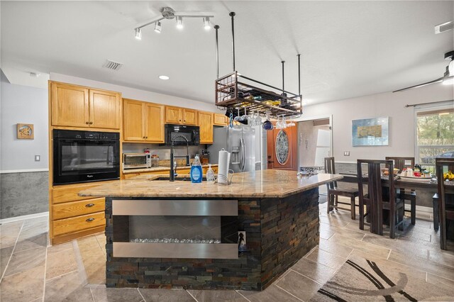 kitchen featuring light stone counters, a sink, visible vents, black appliances, and a center island with sink