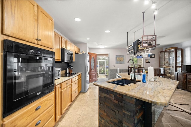 kitchen featuring light tile patterned flooring, a sink, an island with sink, light stone countertops, and black microwave