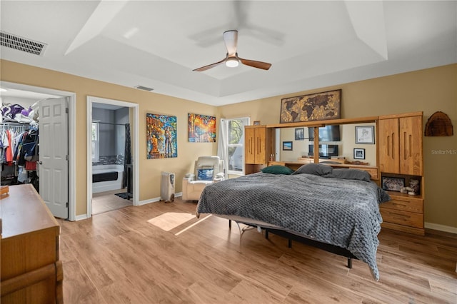 bedroom featuring light wood-type flooring, a tray ceiling, a walk in closet, and visible vents