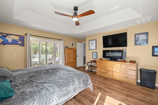 bedroom featuring a tray ceiling, visible vents, light wood-style flooring, access to outside, and baseboards