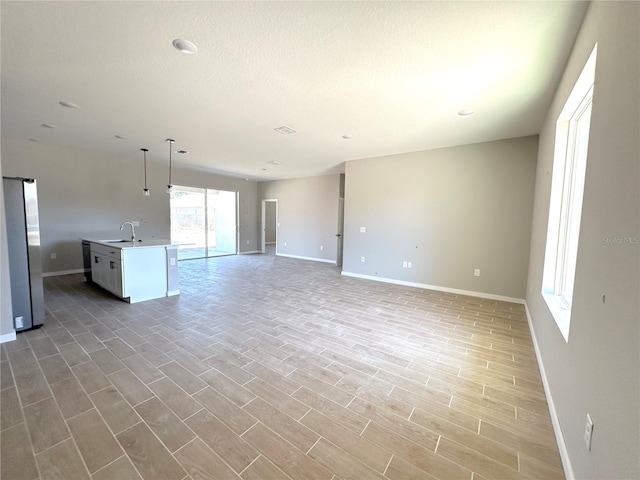 unfurnished living room with baseboards, light wood-style flooring, a sink, and a textured ceiling