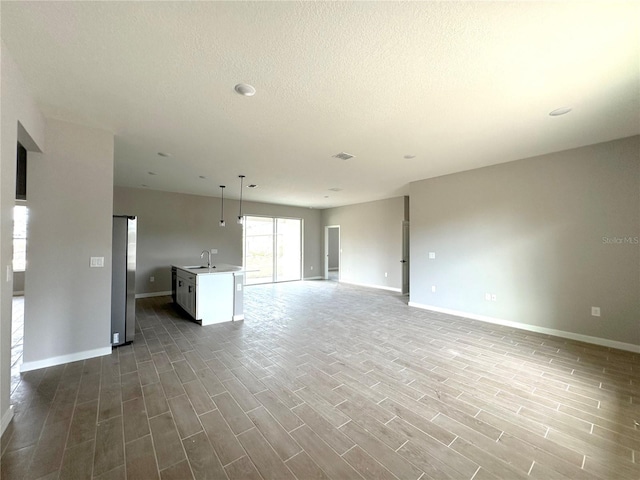 unfurnished living room with wood finish floors, a sink, baseboards, and visible vents