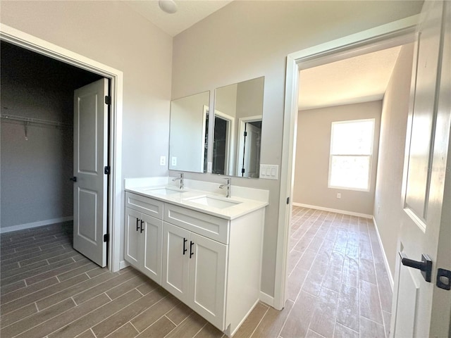full bath with wood tiled floor, double vanity, baseboards, and a sink