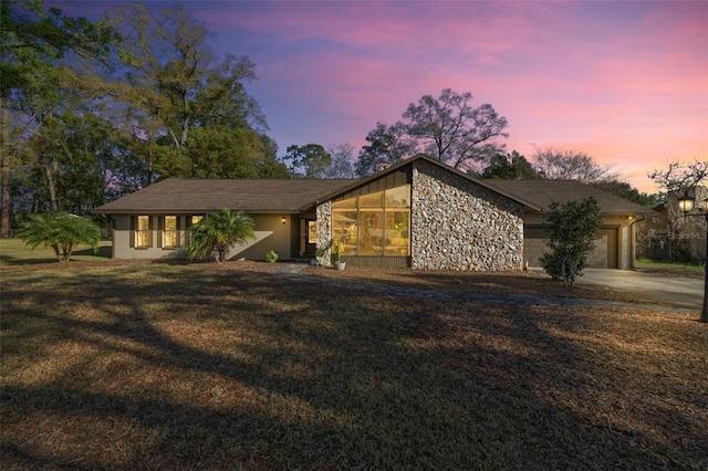 mid-century inspired home featuring a front yard, stone siding, an attached garage, and concrete driveway